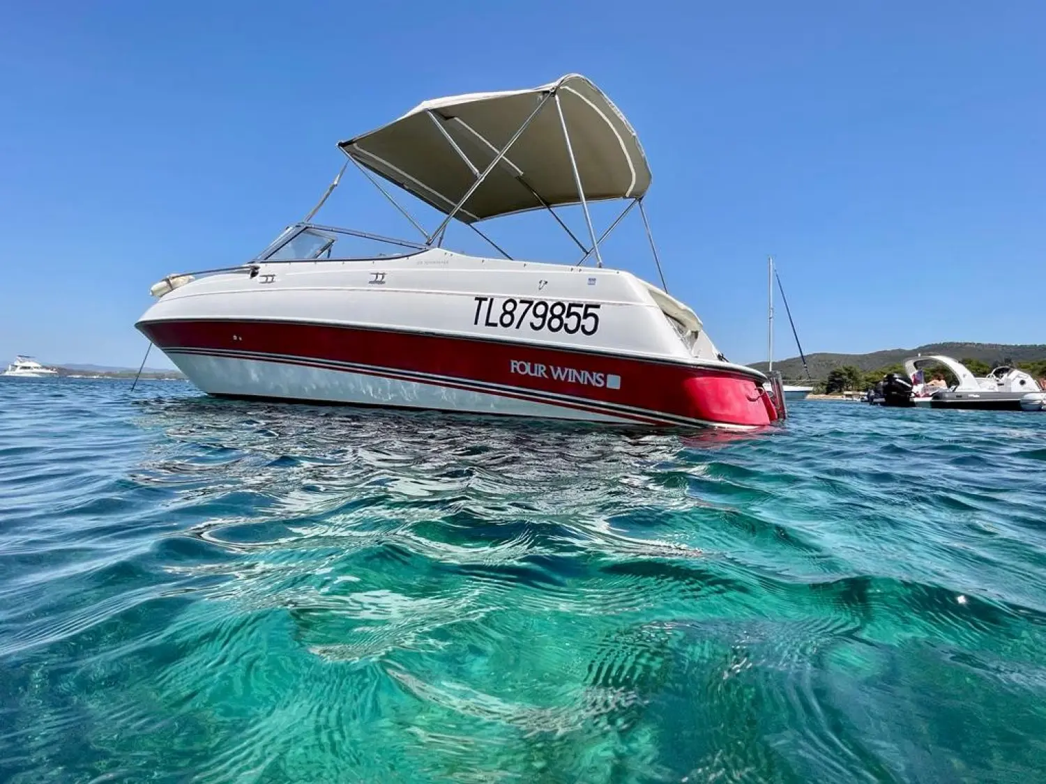 Four Winns Sundowner 235 — Bateau à moteur blanc et rouge photographié au mouillage, vu de trois quarts.