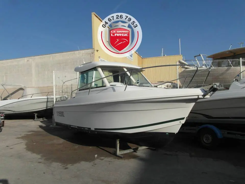 Jeanneau Merry Fisher 625 — Bateau à moteur blanc photographié sur sa remorque devant un bâtiment.