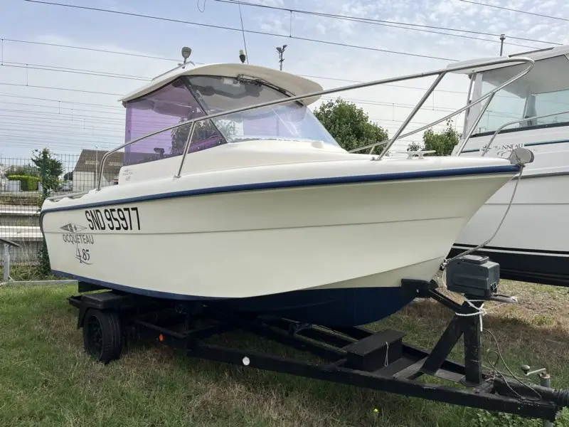 Ocqueteau 485 — Bateau à cabine blanche photographié sur sa remorque, vu de trois quarts avant.