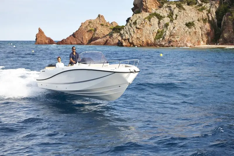 Quicksilver Activ 755 Open — Bateau à moteur blanc naviguant près d’une côte rocheuse.
