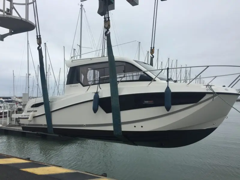 Quicksilver 755 Week-End — Bateau à moteur vu de profil, suspendu par une grue dans une marina.