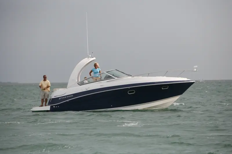 Four Winns V 288 — Bateau à moteur blanc et bleu naviguant, avec deux personnes à bord.