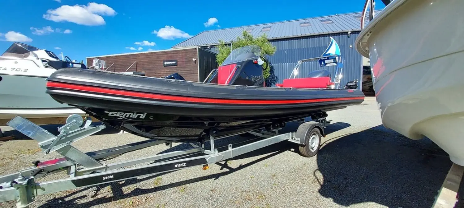 Gemini Waverider 650 — Bateau pneumatique noir et rouge présenté sur sa remorque devant un bâtiment.