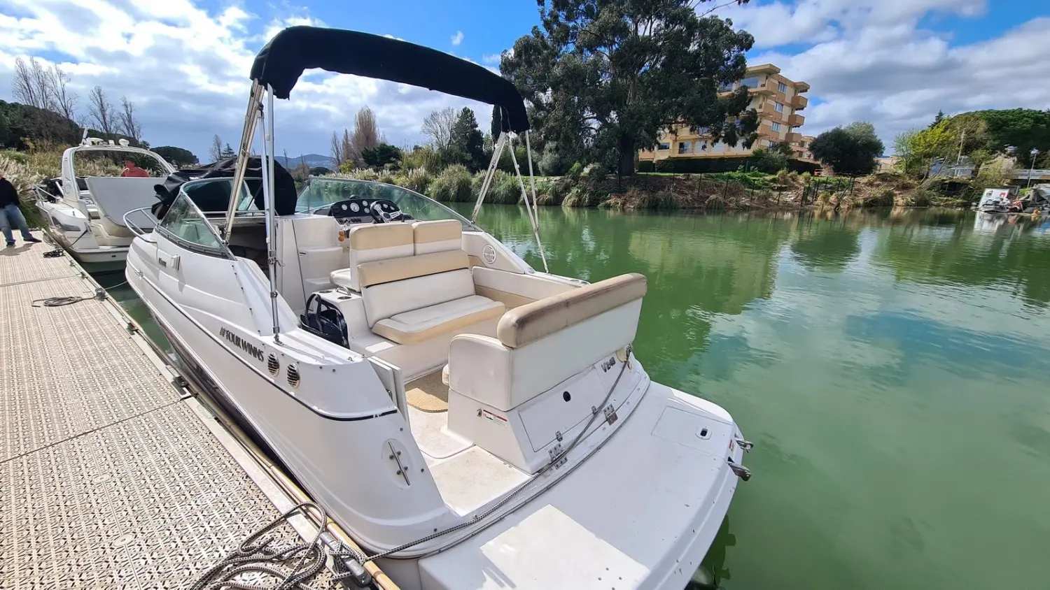 Four Winns Vista 248 — Bateau blanc amarré, vu de trois quarts arrière, avec taud noir et plateforme arrière.