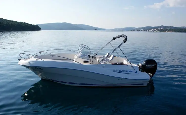 Quicksilver 635 Commander — Bateau à moteur blanc photographié au mouillage dans une baie calme.